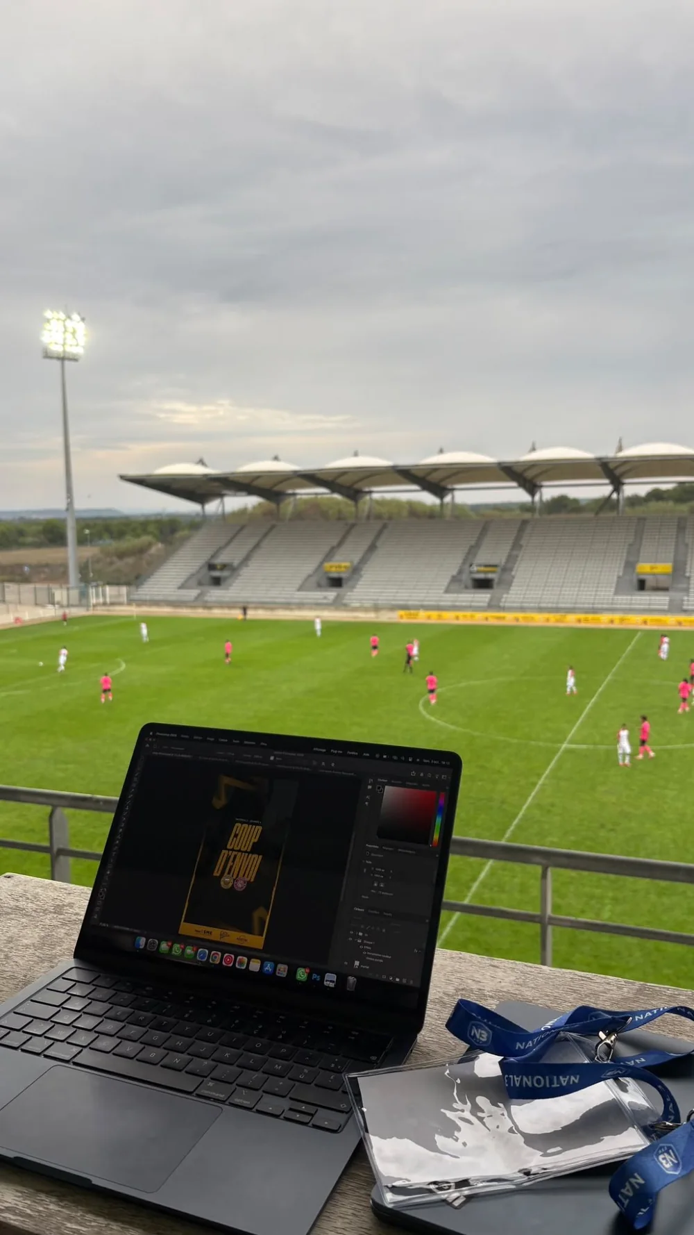 Ordinateur avec un visuel « Coup d’envoi » en cours de création, face à la pelouse du stade